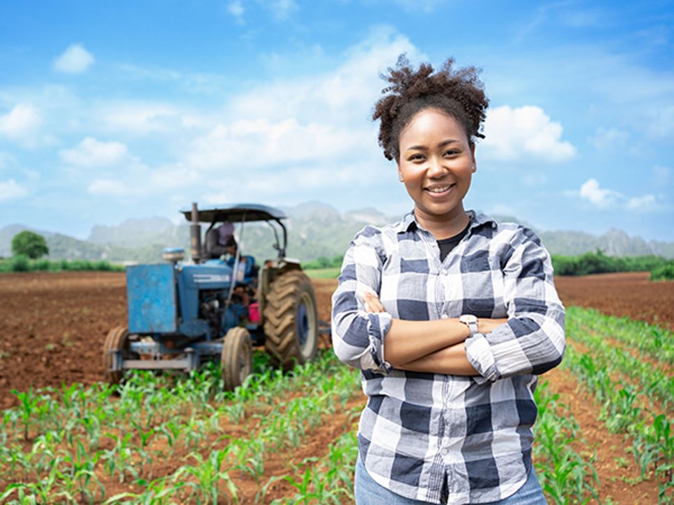 Woman farmer in field on a farm with a tractor inspecting crops.
