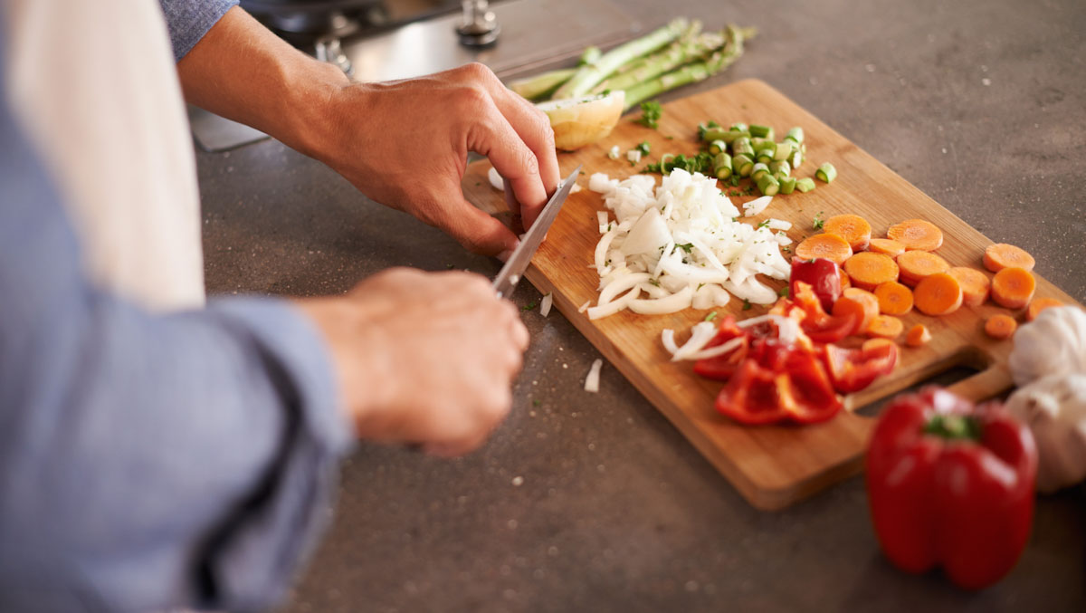 Close up of someone's hands chopping a variety of vegetables on a cutting board.
