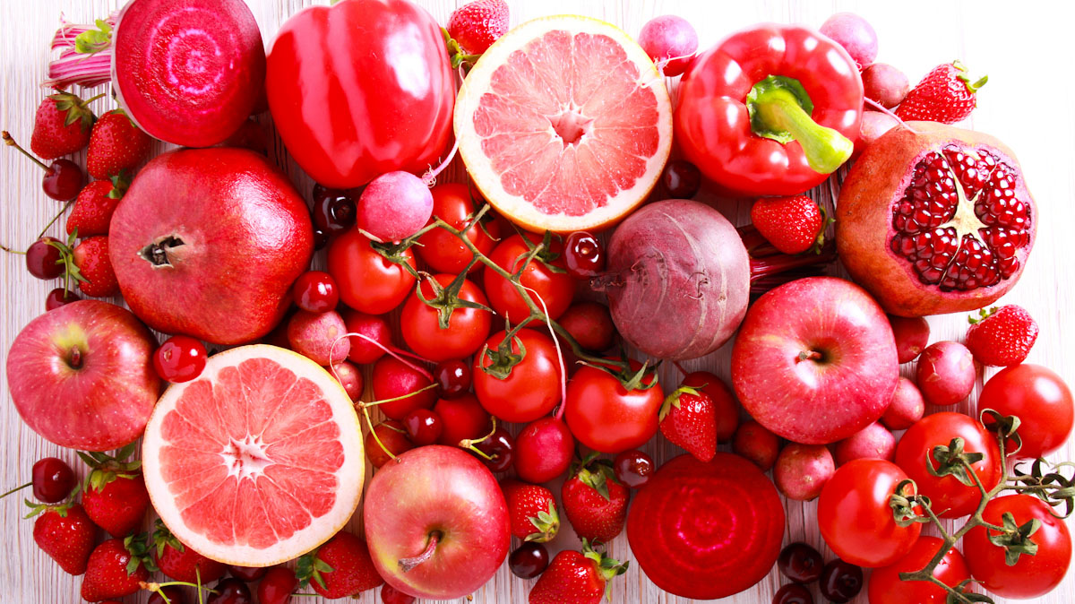 An assortment of red and pink, fruits and vegetables. Including: grapefruit, pomegranates, tomatoes, blood oranges, apples, cherries and strawberries.