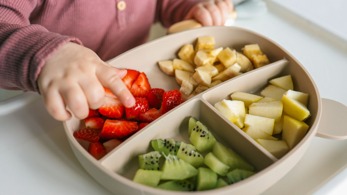 A baby's hand picks up pieces of cut strawberry.