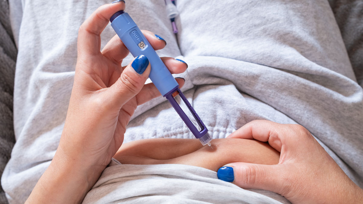 Close up of a woman giving herself a GLP-1 injection to her stomach.