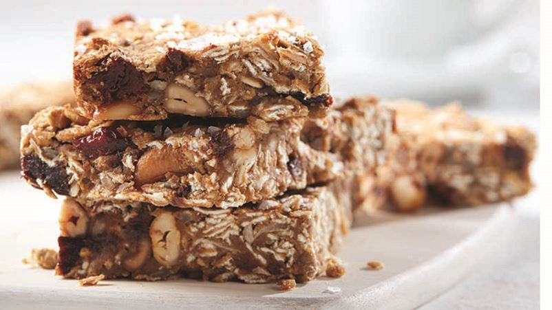 A plate of a stack of three cannellini cashew breakfast bars with a couple in the back.