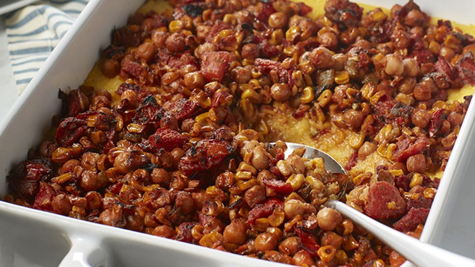 A white, square dish with chickpea cornmeal casserole and a metal serving spoon scooping some to serve.