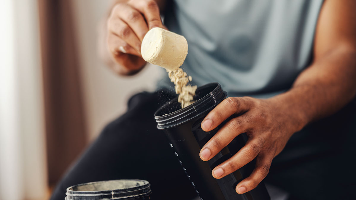Close up of a man's hands scooping powder into a cup before a workout.