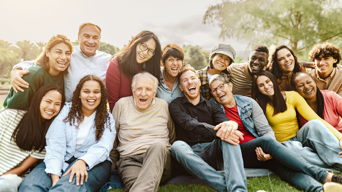 Intergenerational group of people, smiling and sitting on the grass.