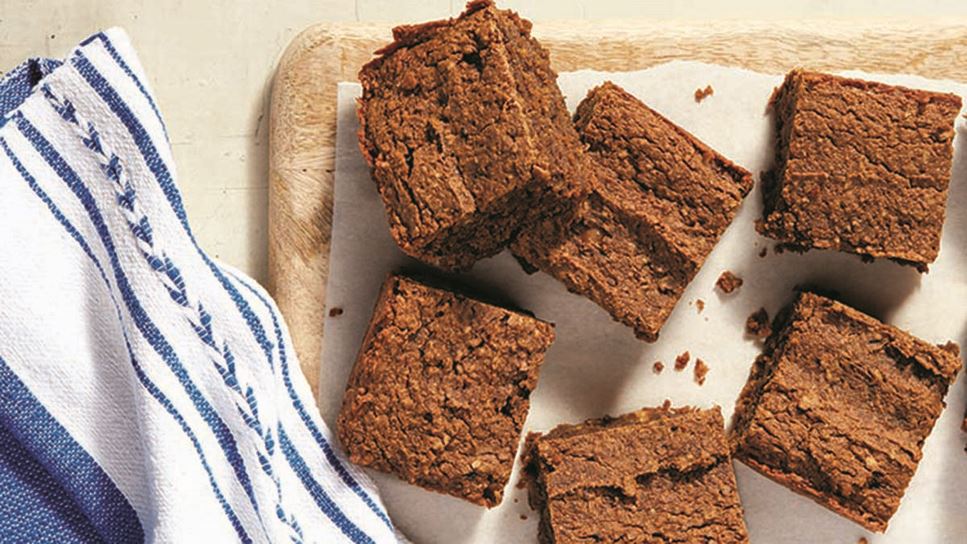 A plate holding six brownies next to a blue and white cloth napkin.