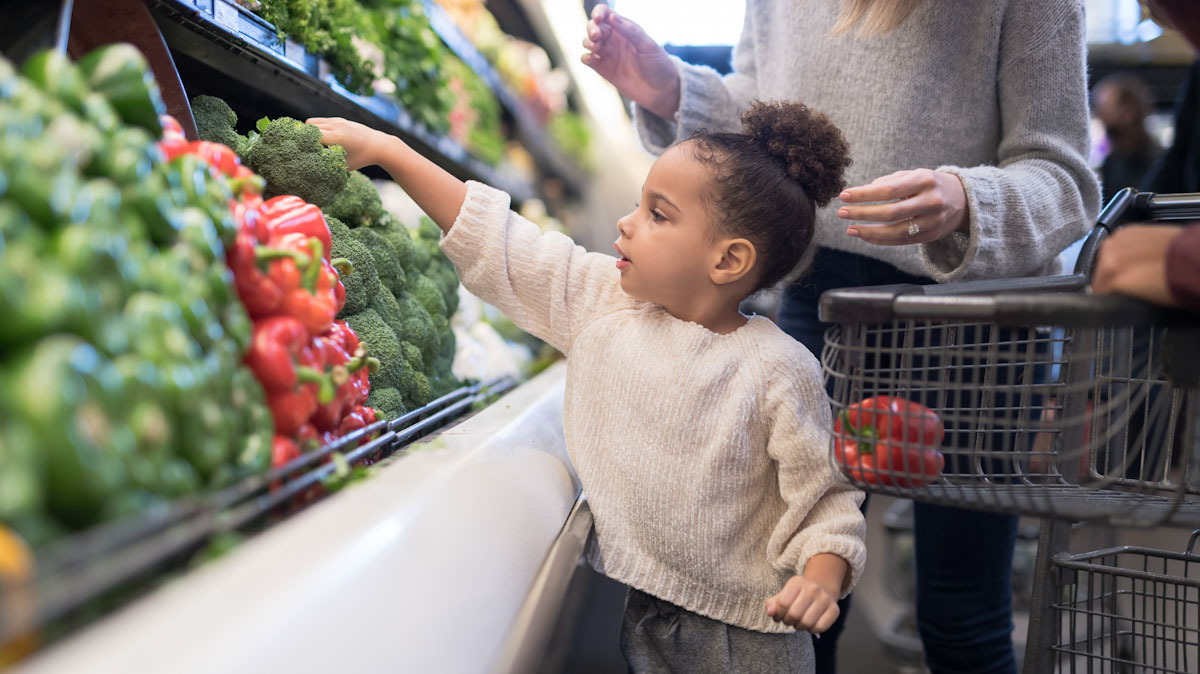 A small child shops for produce with her mother and father at the grocery store.