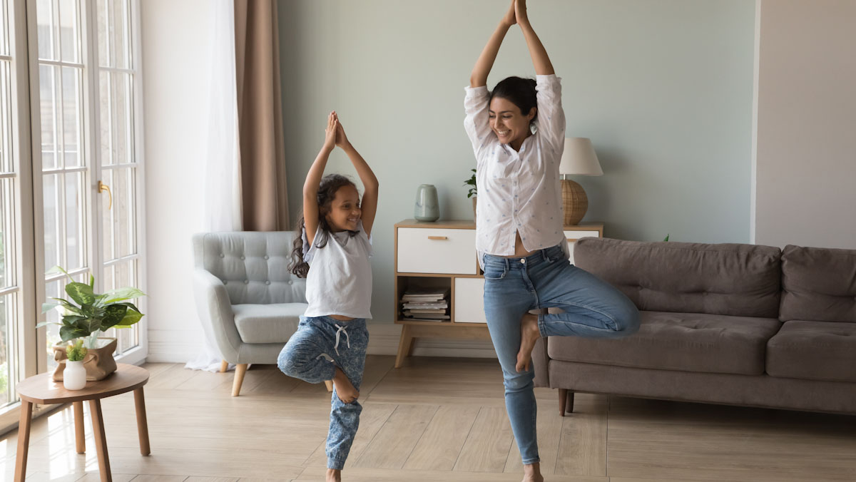 A mother and daughter do yoga in their living room.