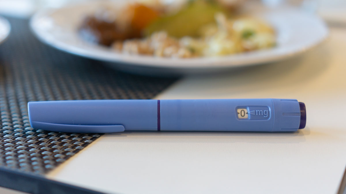 An ozempic injection pen sits next to a plate of food.