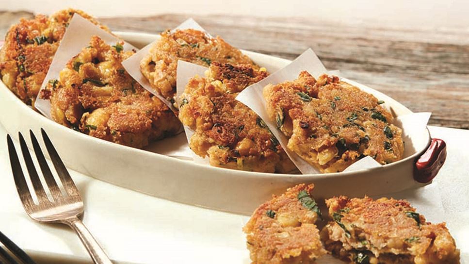 A serving dish of five chickpea fritters divided by piece of paper with two forks and a fritter broken in half in the foreground. 