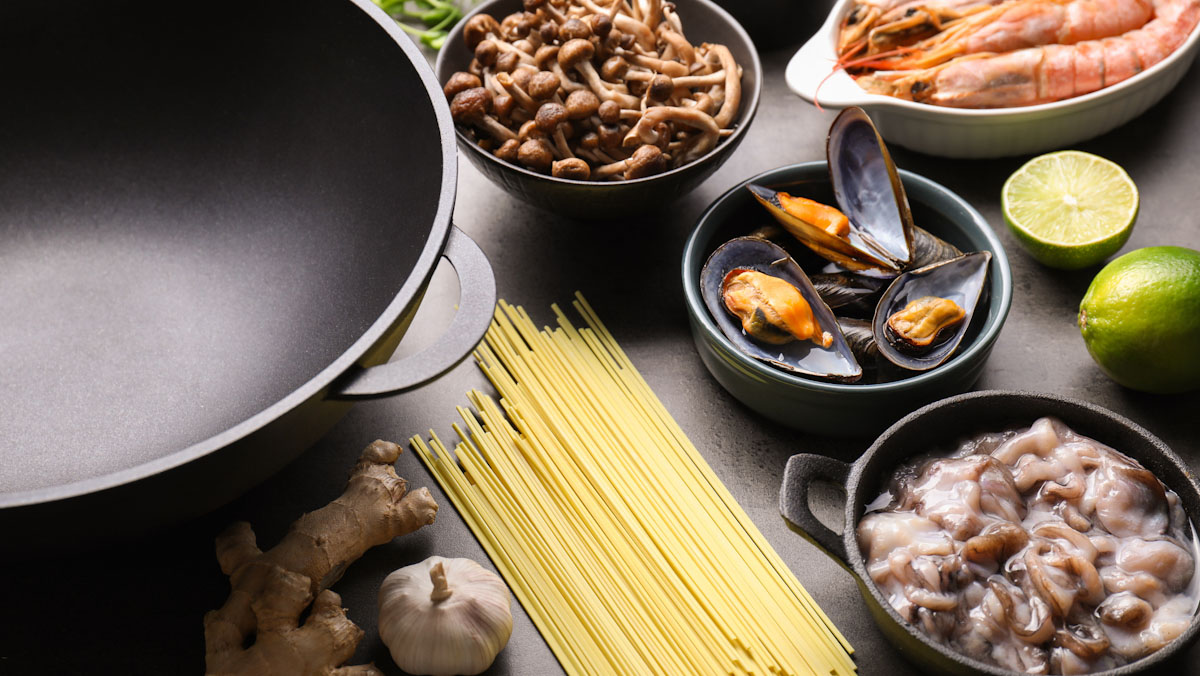 Prawns, mushrooms, noodles, mussels, lime, garlic and ginger sit next to an empty wok.