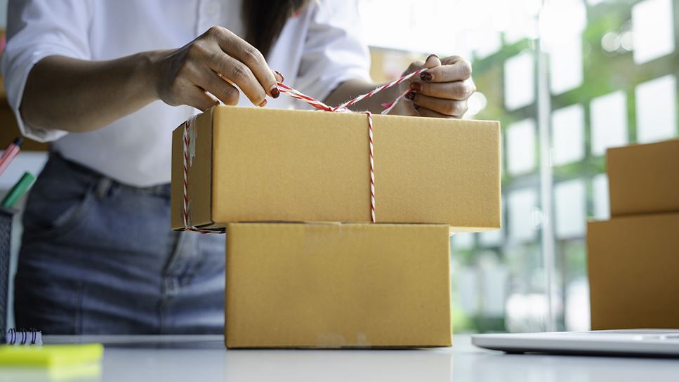 Woman tying a ribbon around a box to demonstrate mailing homemade food gifts.