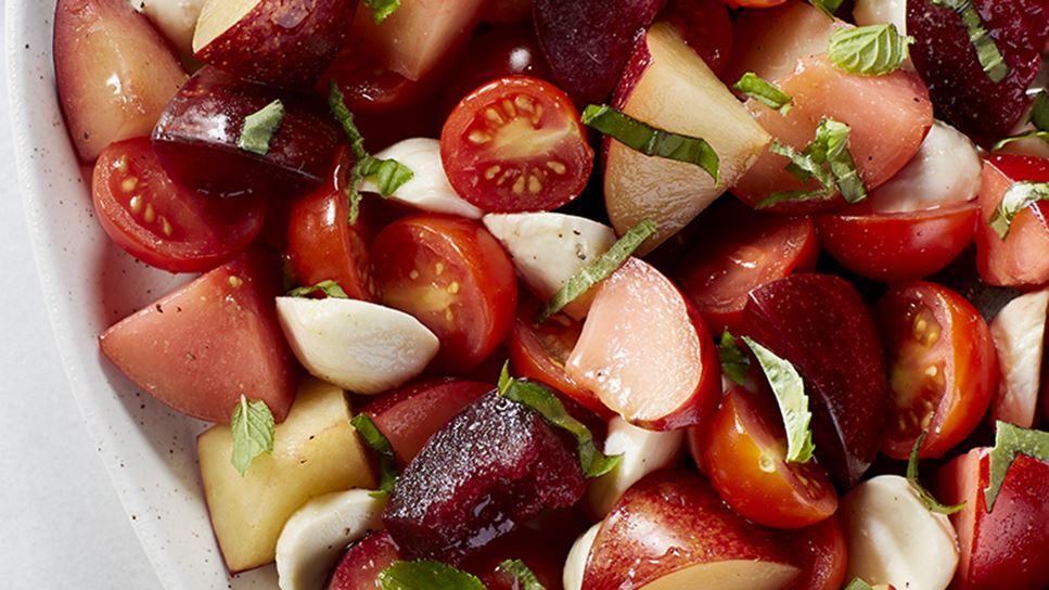 A bowl of salad filled with chunks of tomatoes, plums and mozzarella cheese sprinkled with bits of fresh basil. 