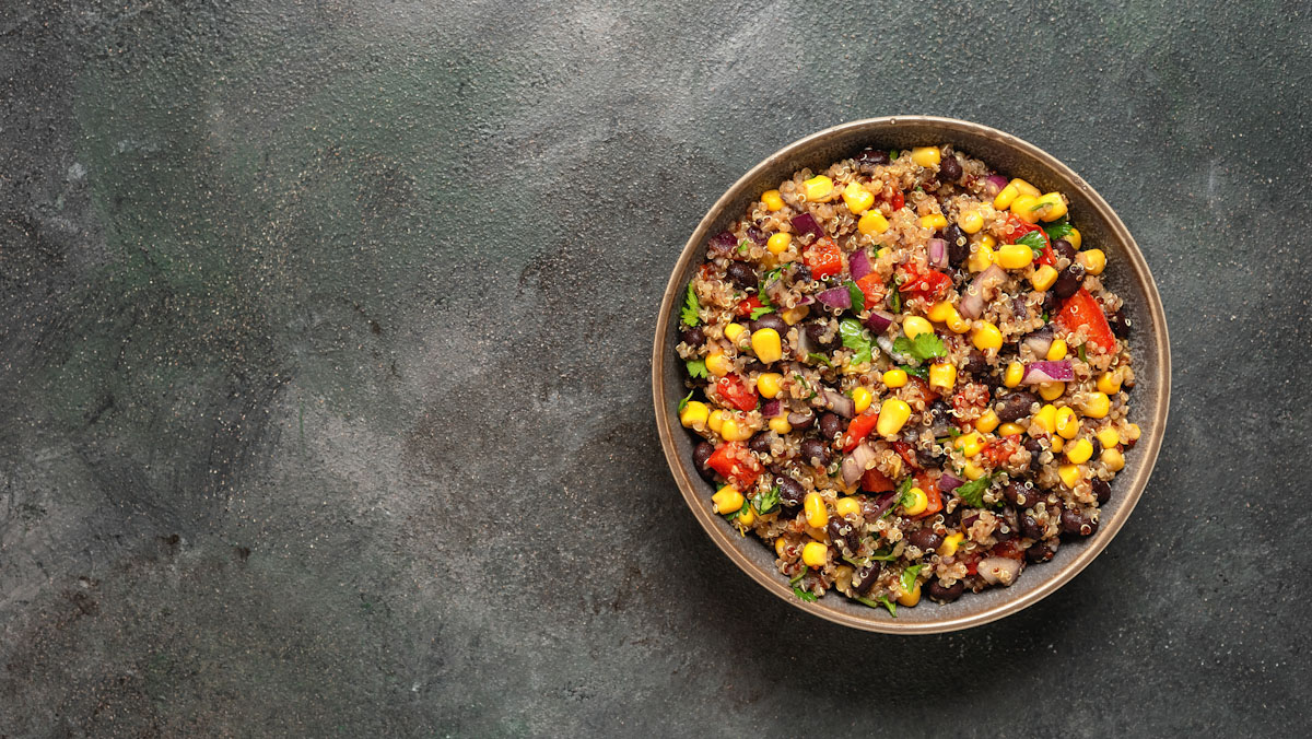 A bowl of corn, black bean, and quinoa salad on a dark table.