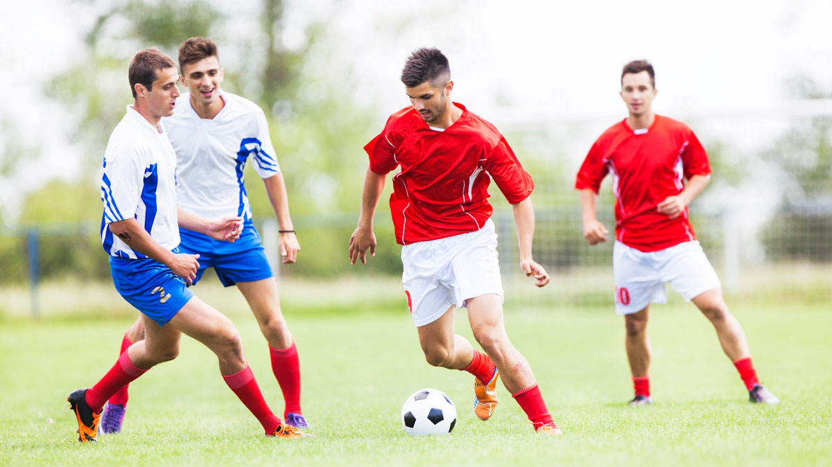 A team of male athletes kick a soccer ball outside.