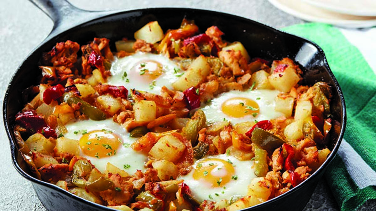 A cast iron pan full of tuna hash with four sunny-side up eggs on top. 