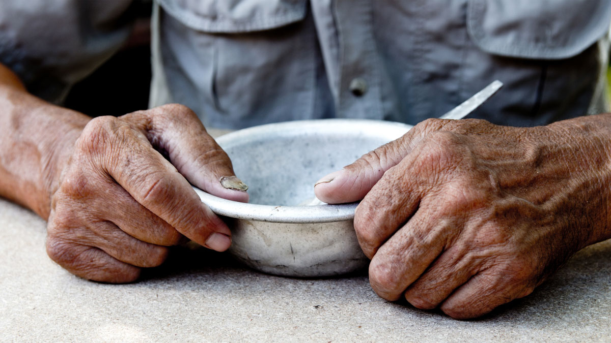 An emaciated man's hands hold an empty bowl.