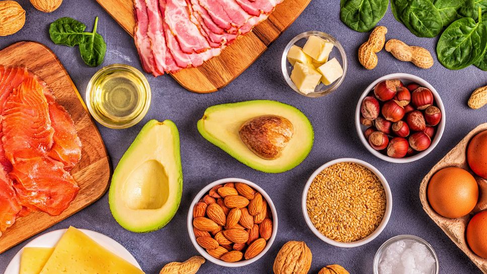 An assortment of high fat and low carbohydrate foods, including avocado, bacon, nuts, cheese, oil, butter and salmon.