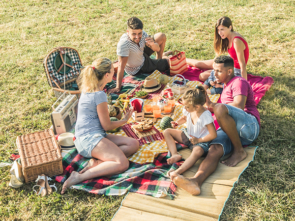 Group of people outside on picnic blankets having a picnic and safely eating their favorite healthy foods outside.