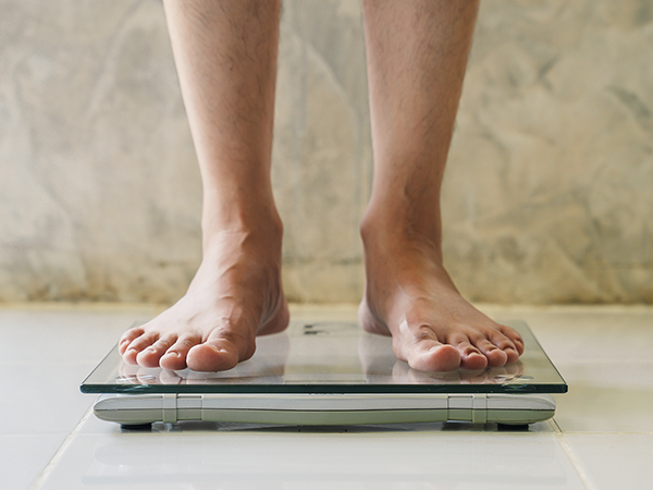 Man with an eating disorder standing on a scale showing that disordered eating can affect men and boys.