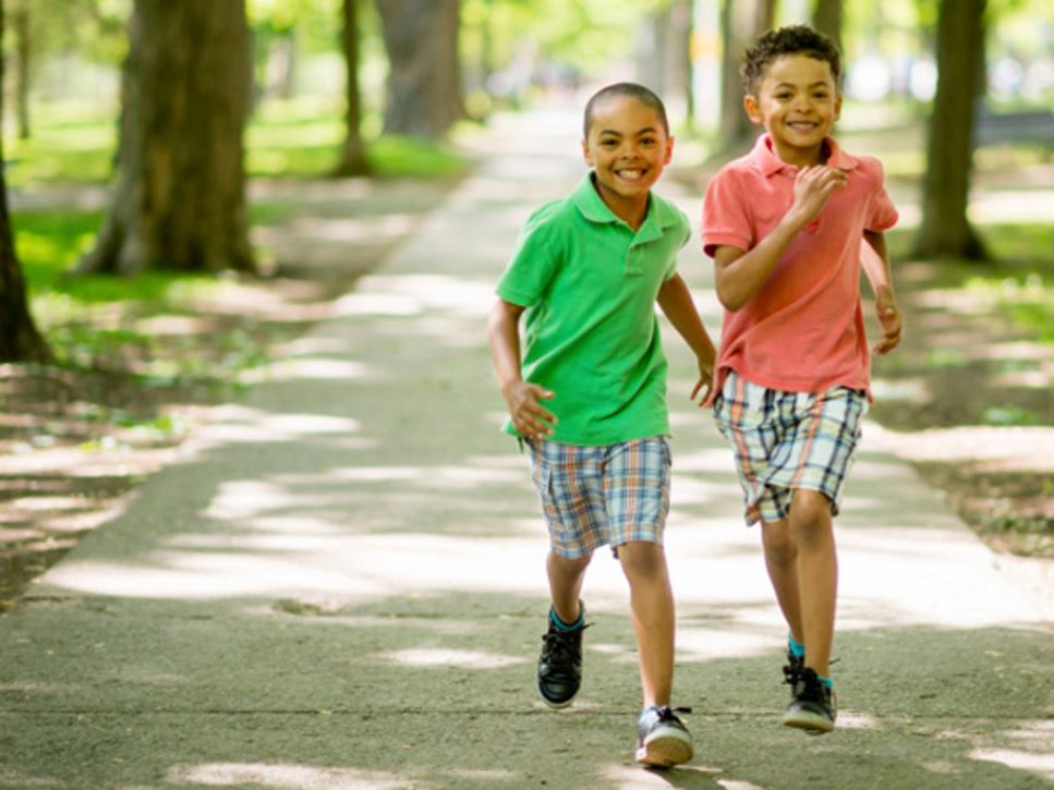 Two young boys wearing fitness trackers running outside