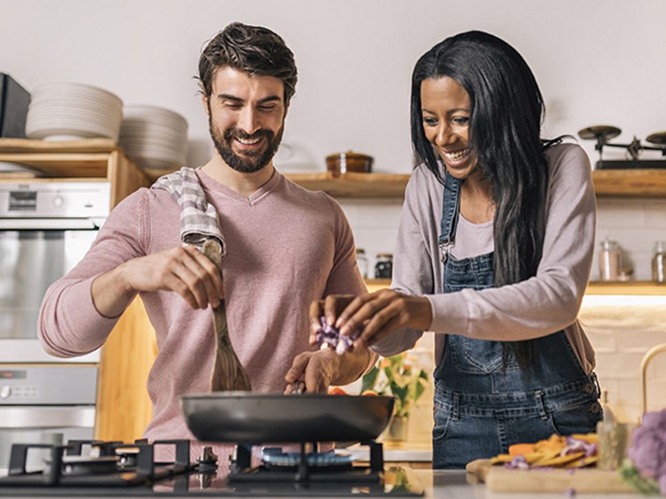 A couple smiling and cooking food for lunch together in the kitchen at home.