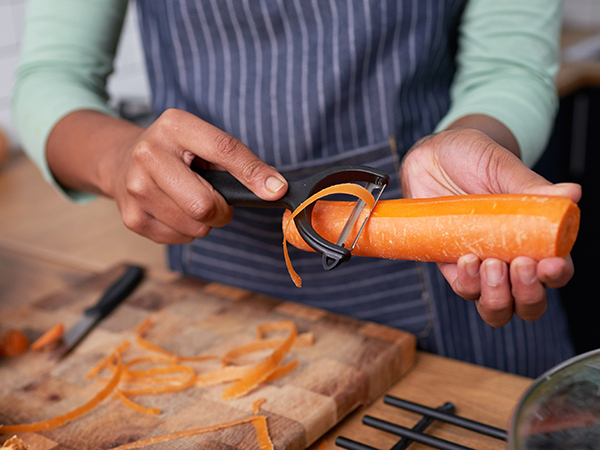 Woman peeling a carrot with a vegetable peeler.