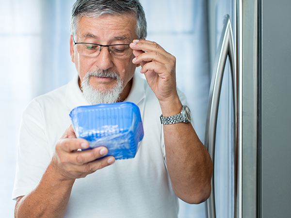 Man looking at food label on mushrooms in his refrigerator to see if they are expired or have a best by/use by date.