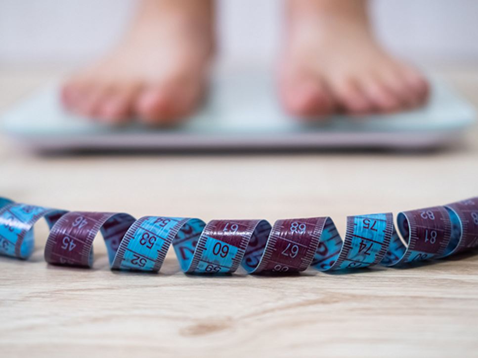 Person with an eating disorder standing on a scale near a body measuring tape.