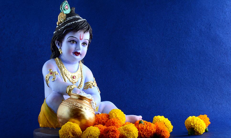 Hindu God Krishna sits with a butter pot and flowers to represent the Krishna Janmashtami celebration.