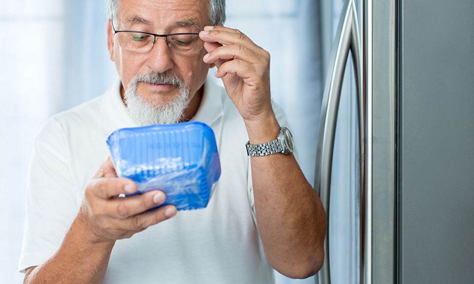 Man looking at food label on mushrooms in his refrigerator to see if they are expired or have a best by/use by date.