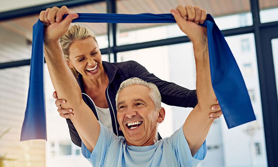 older man using a resistance band with a woman trainer helping