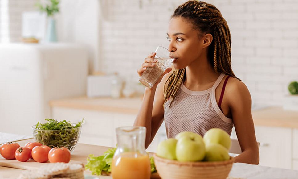 woman drinking water with healthy foods on counter